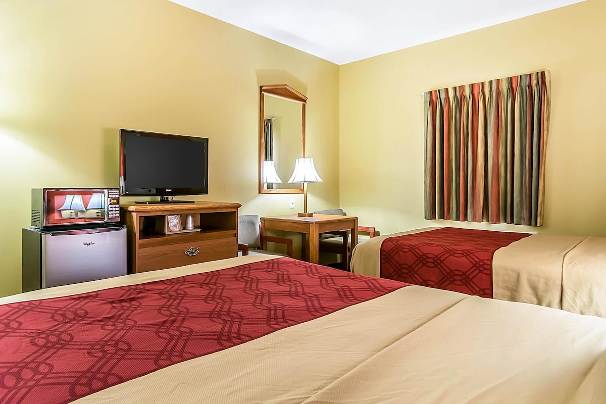 Een hotelkamer met twee bedden, een televisie, een bureau met lamp, een magnetron en een dressoir.