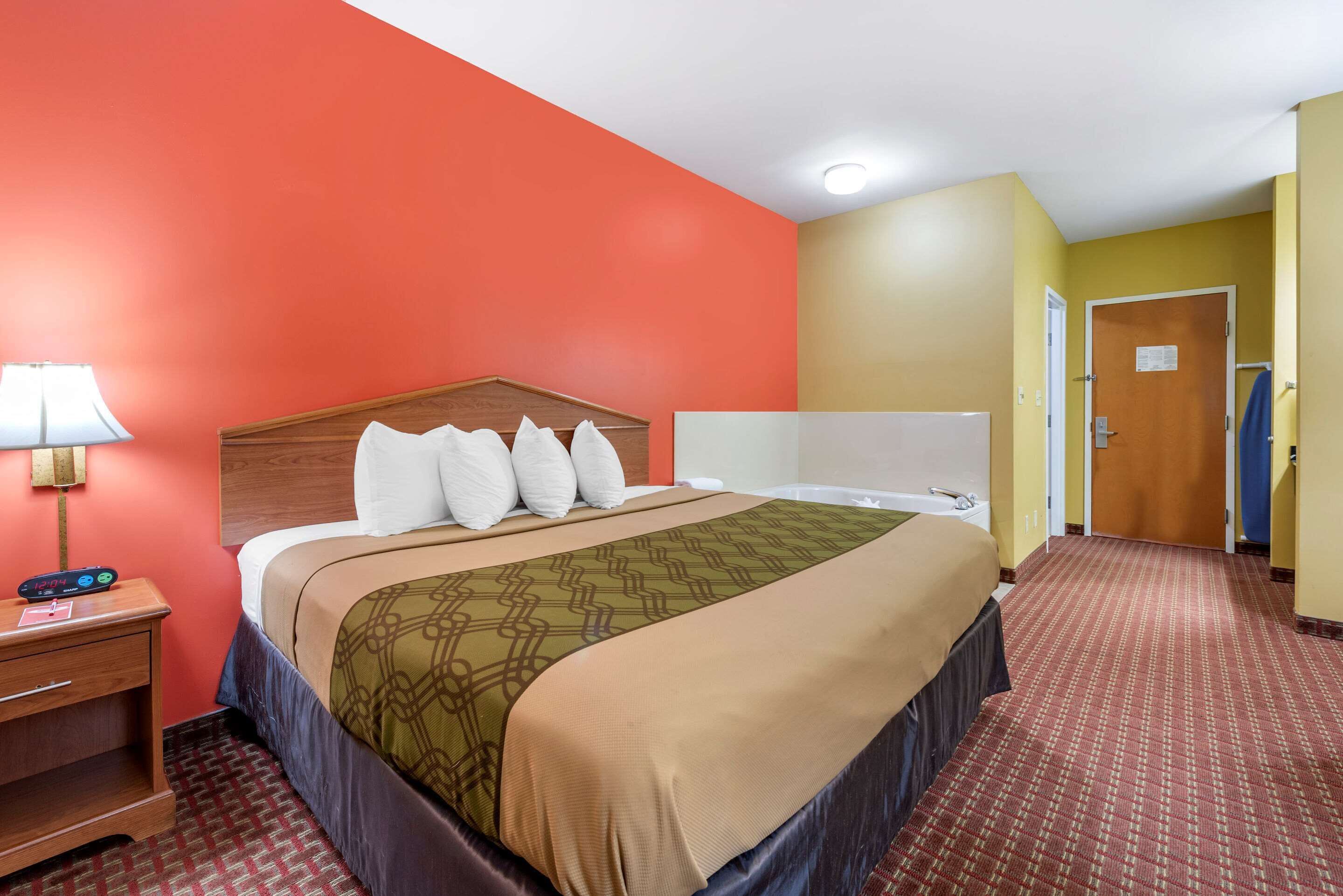 A hotel room with a bed, a nightstand, a lamp, and a door.
