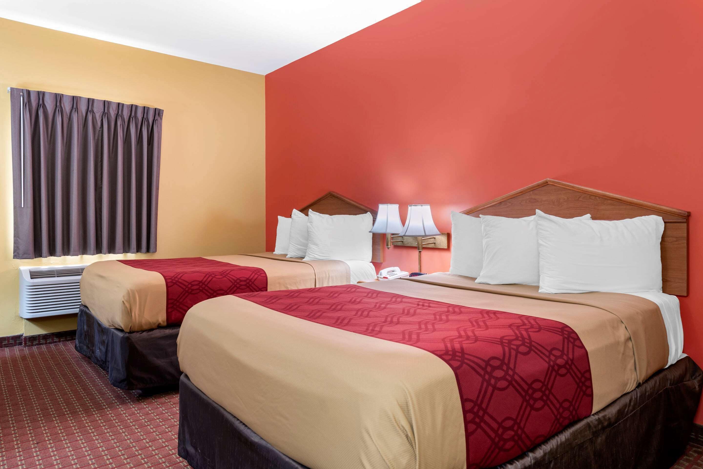 A hotel room with two beds, a red wall, and a window with curtains.