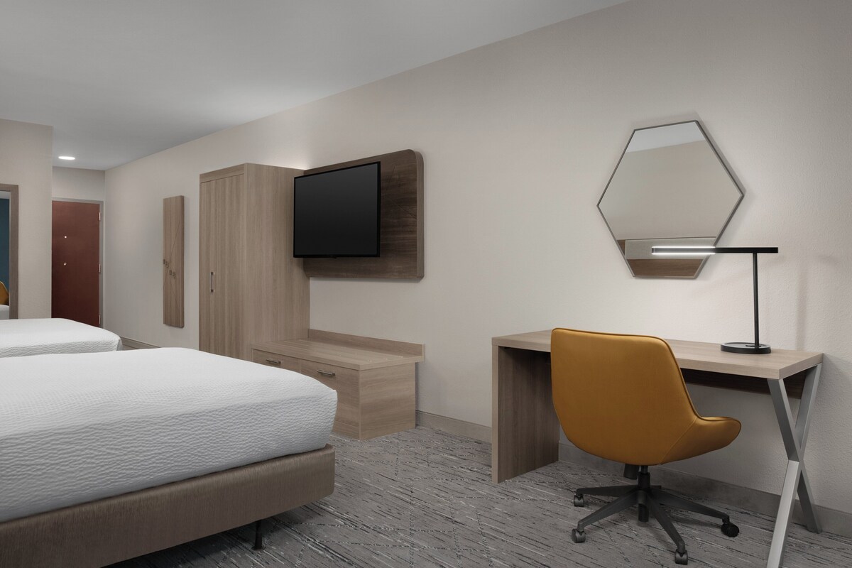 A hotel room with two beds, a desk, a chair, a TV, and a mirror.