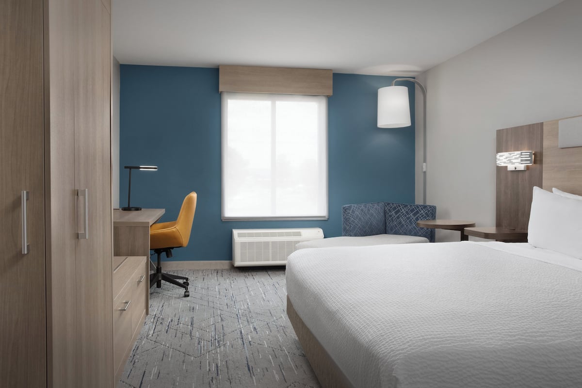 Une chambre d’hôtel équipée d’un lit, d’un bureau, d’une chaise et d’une fenêtre avec des stores.