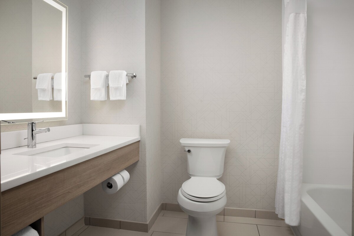 A modern bathroom with a white sink, mirror, toilet, and shower curtain.