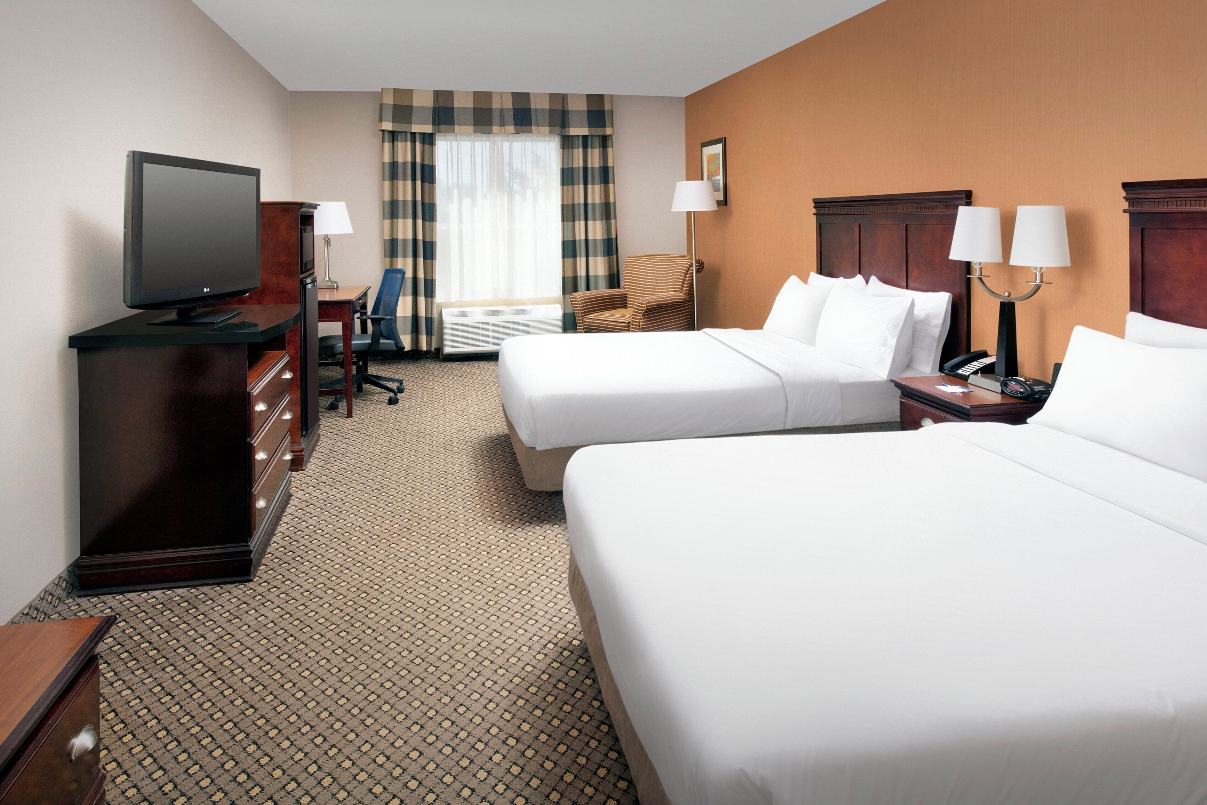 A hotel room with two beds, a desk with a television, a chair, and a lamp.