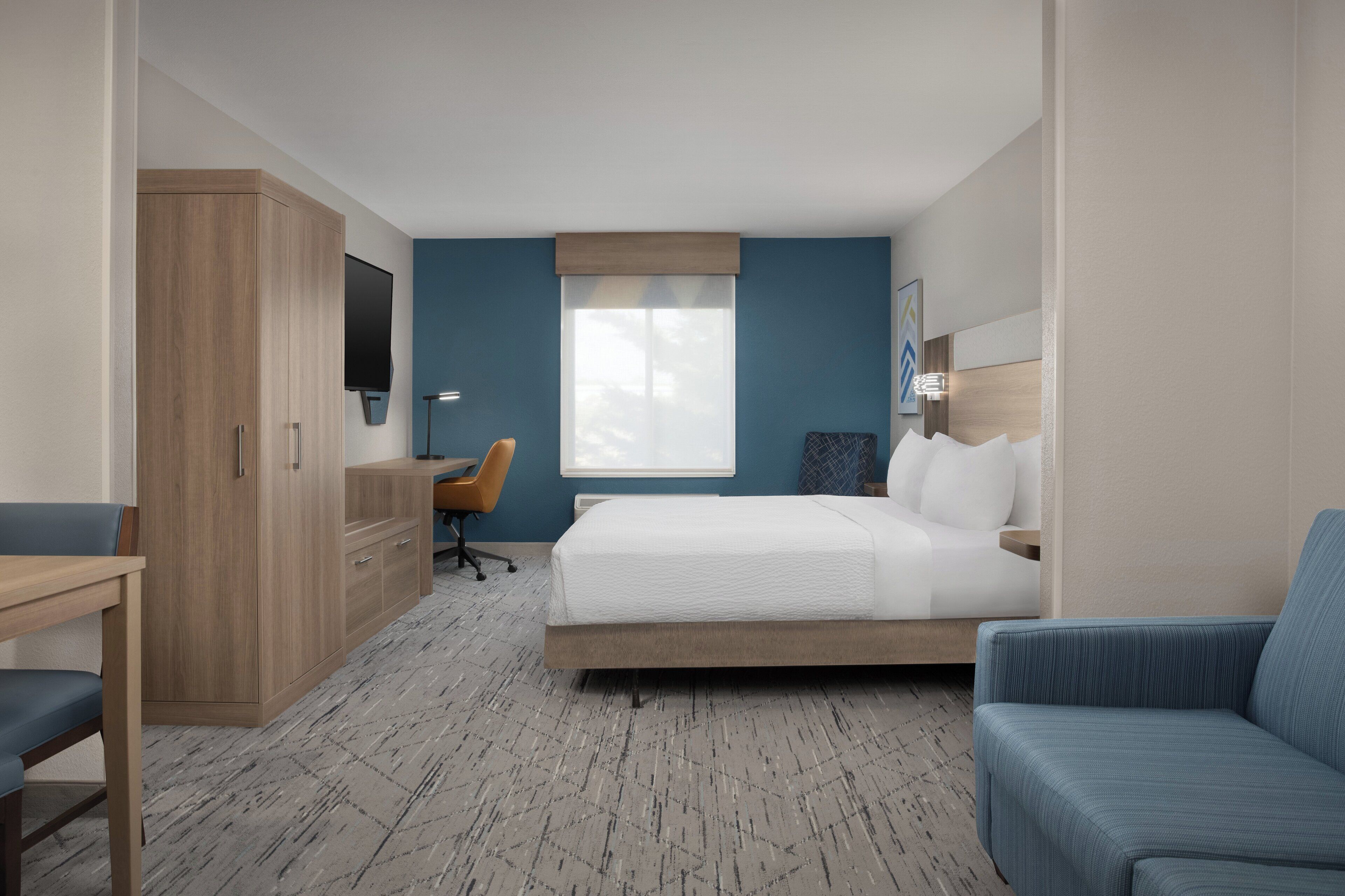 A hotel room with a bed, a desk, a chair, a wardrobe, and a television.