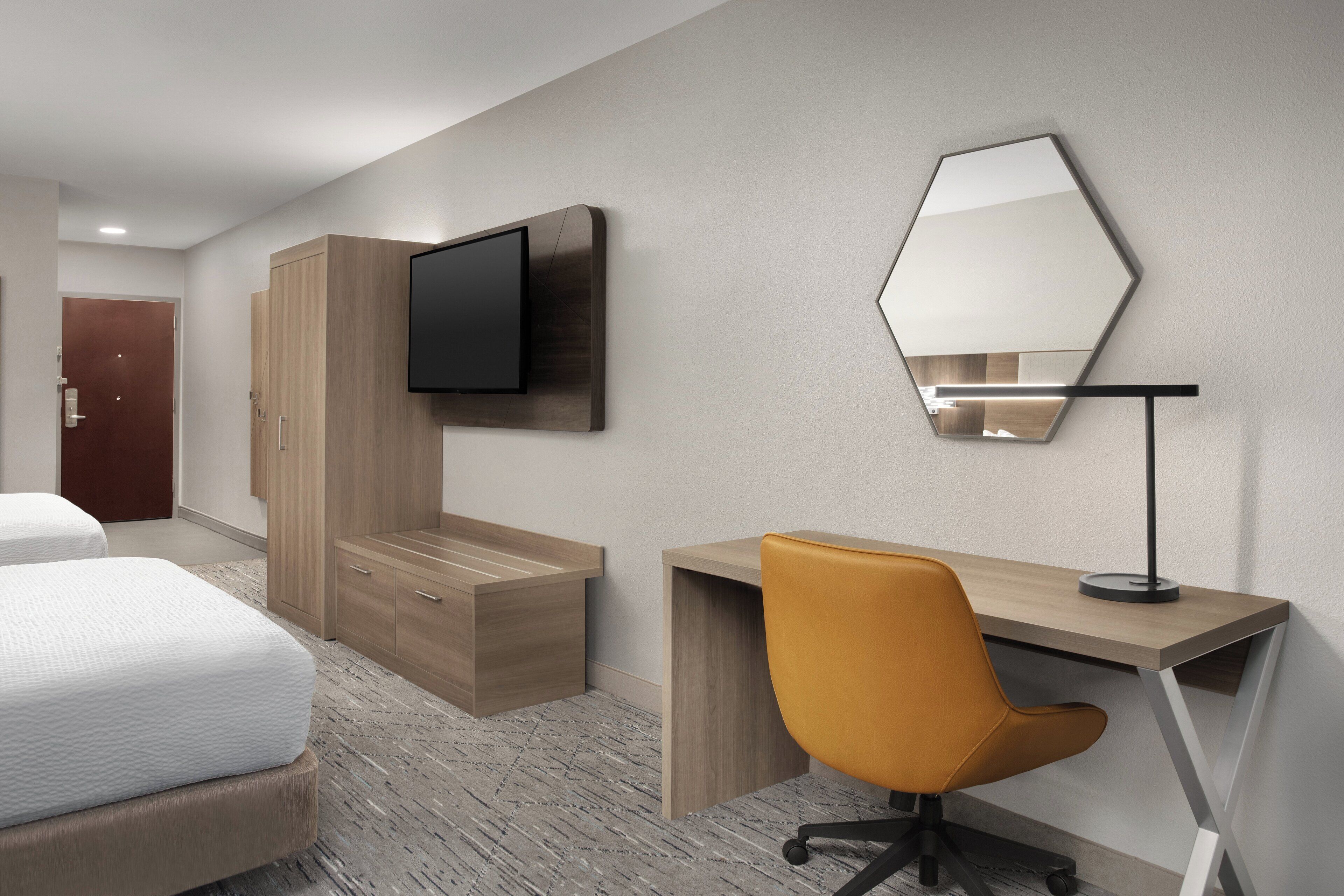Une chambre d’hôtel avec un lit, un bureau, une chaise, une télévision et un miroir.