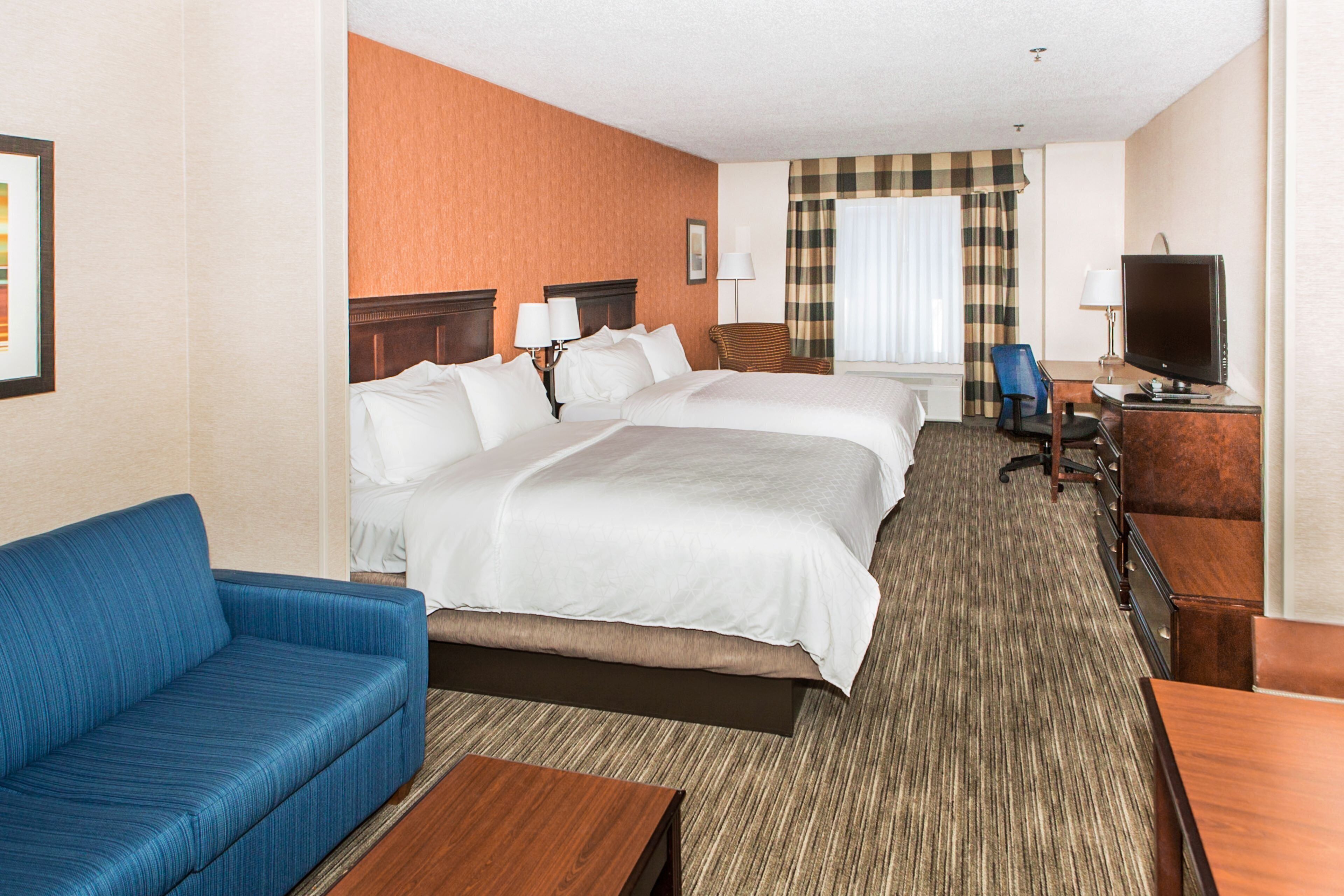 A hotel room with a large bed, a blue sofa, a desk with a computer, and a television.