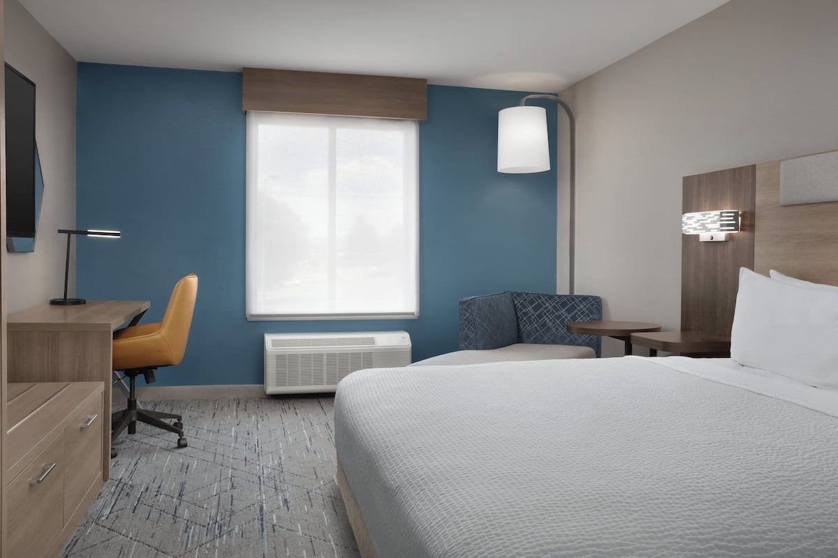 Une chambre d’hôtel équipée d’un lit, d’un bureau, d’une chaise, d’une fenêtre et d’une lampe fixée au mur.