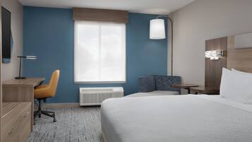 A hotel room with a bed, a desk, a chair, a window, and a wall-mounted lamp.