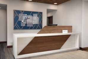 Un comptoir d’accueil au design moderne, une œuvre d’art murale géométrique aux couleurs bleu et blanc au-dessus, et un élément décoratif en bois sur le comptoir.
