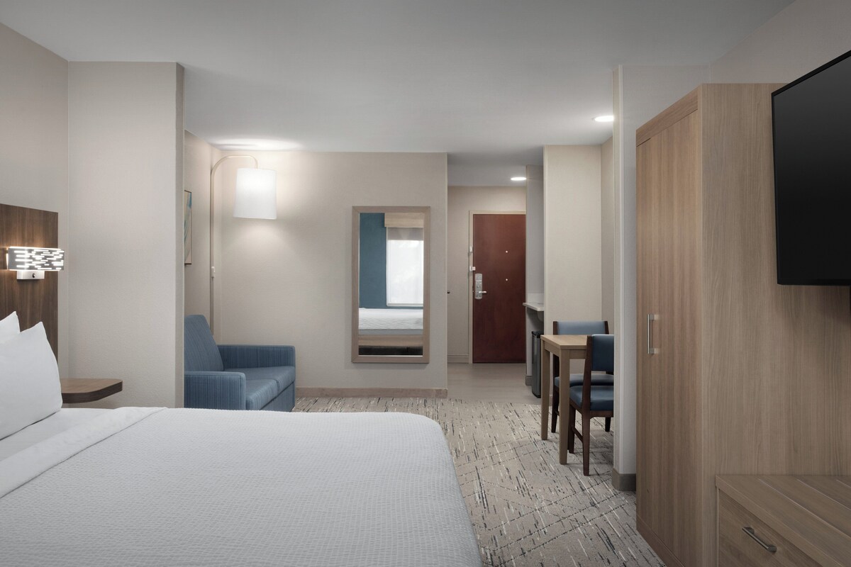 A hotel room with a large bed, a desk, a chair, a wardrobe, and a television.