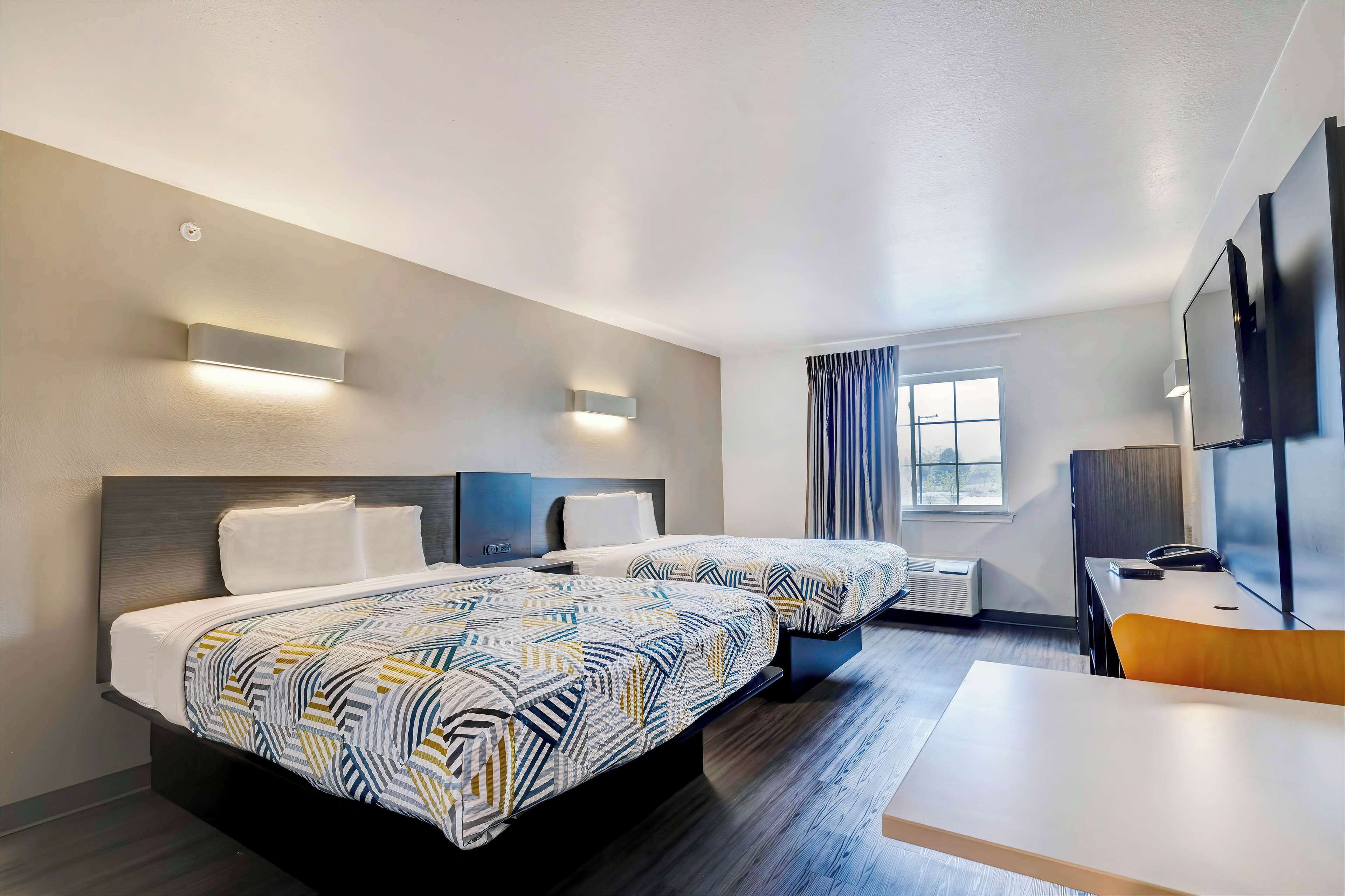 Habitación de hotel con dos camas, un escritorio, una silla, un televisor y una ventana con cortinas.