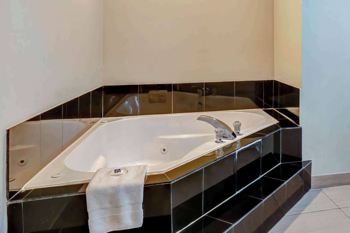 A modern bathroom with a large freestanding bathtub, black tiled walls, and a white towel on the floor.