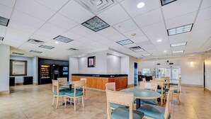 A spacious indoor area with multiple tables and chairs, a reception desk, and a counter with a display. - Motel 6 Mesquite, TX - Balch Springs (Balch Springs)