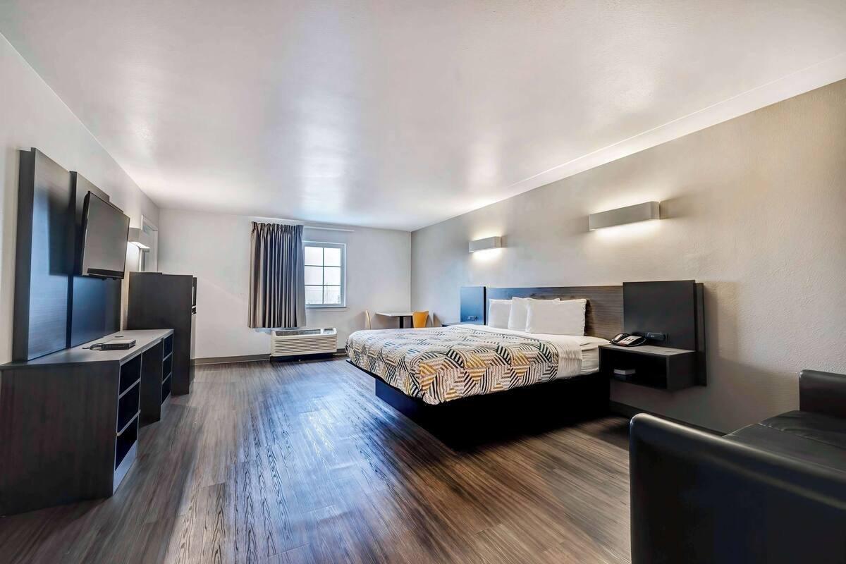 A modern hotel room with a large bed, a desk, a flat-screen TV, and a window with curtains.