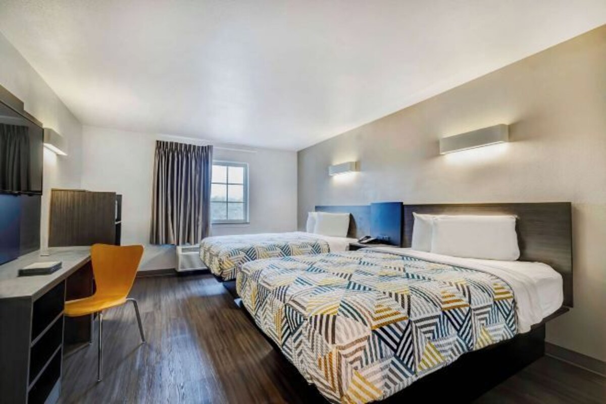 A hotel room with two beds, a desk, a chair, and a large window.