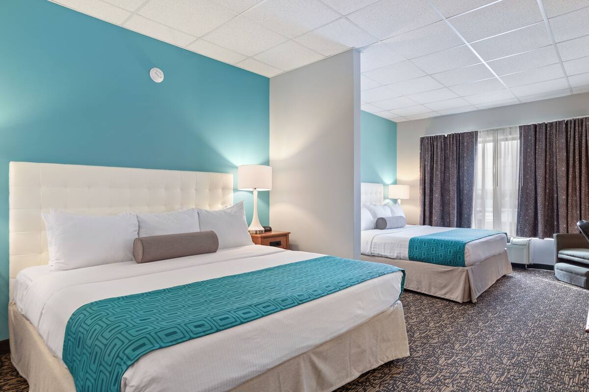 Ein Hotelzimmer mit zwei Betten, einer Wanduhr und einem mit Vorhängen versehenen Fenster.