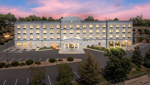 A multi-story hotel with a central entrance, parking lot, and surrounding greenery. - Elevation Inn & Suites, Trademark Collection by Wyndham (Rapid City)