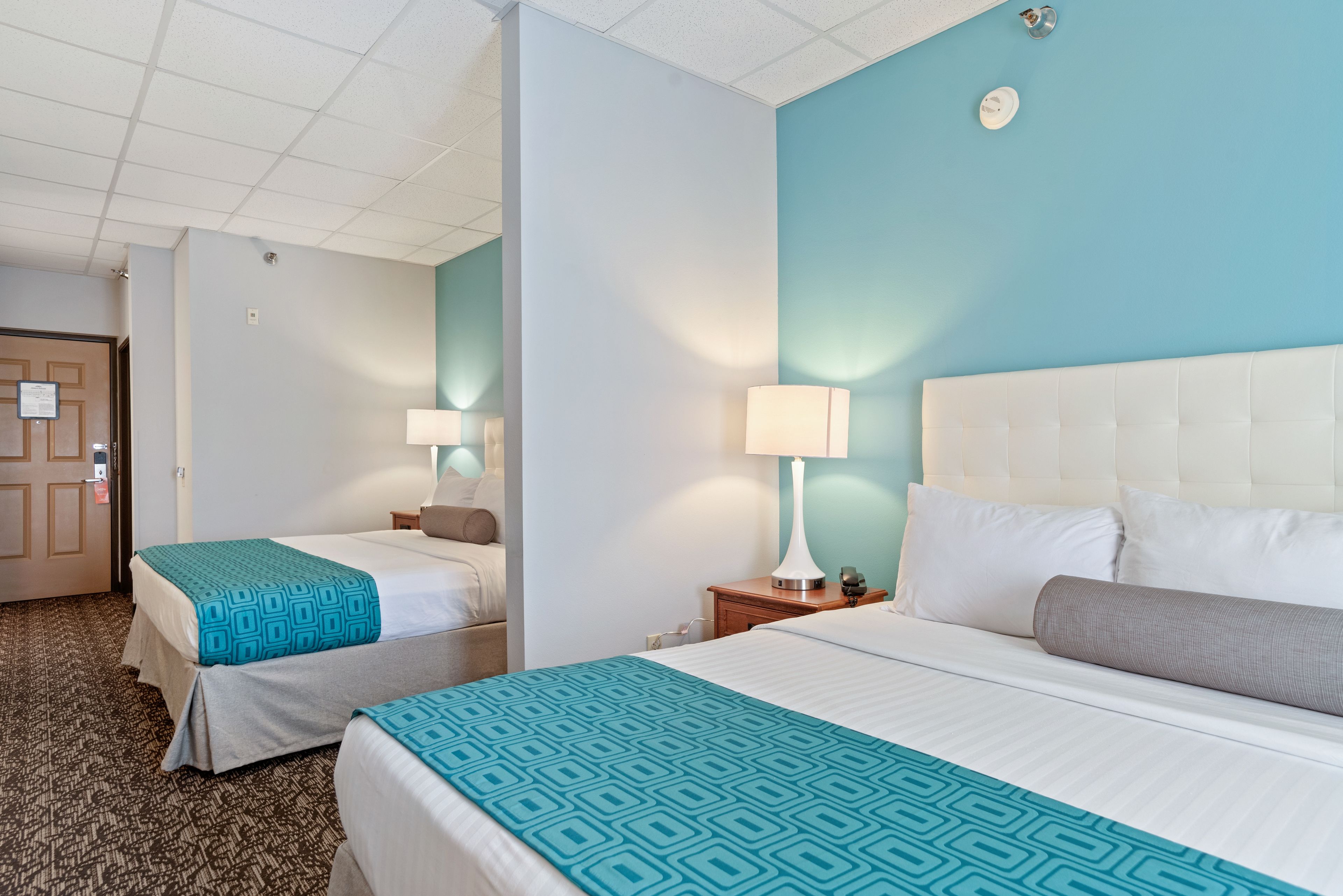 A hotel room with two beds, a white headboard, a teal accent wall, and a patterned bedspread.