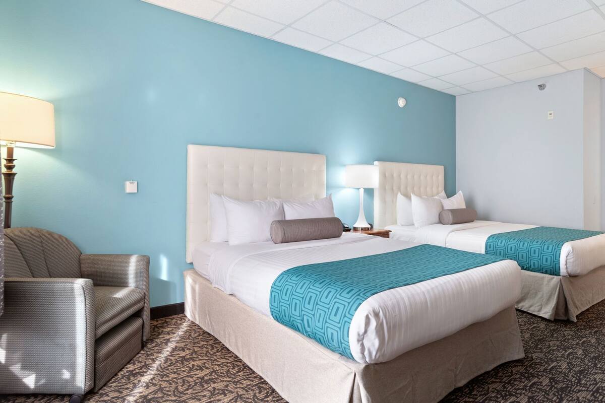 Ein Hotelzimmer mit zwei Betten, einem Sessel und einer Lampe.