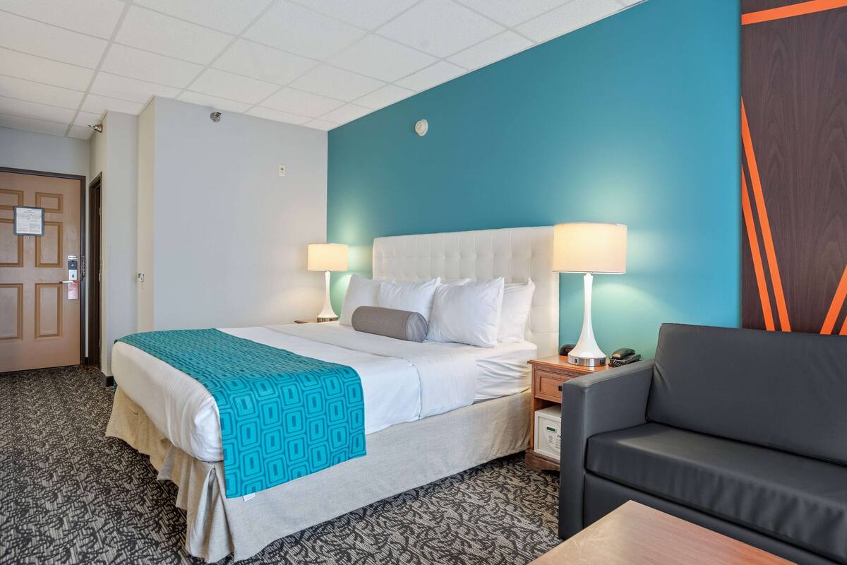 Ein Hotelzimmer mit einem Bett, zwei Nachttischlampen, einem grauen Sofa und einem Holznachttisch.