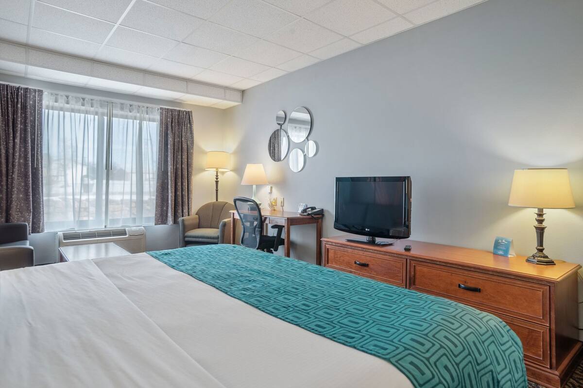 Ein Hotelzimmer mit Bett, Schreibtisch mit Fernseher, Stuhl, Lampe und einem Fenster mit Vorhängen.