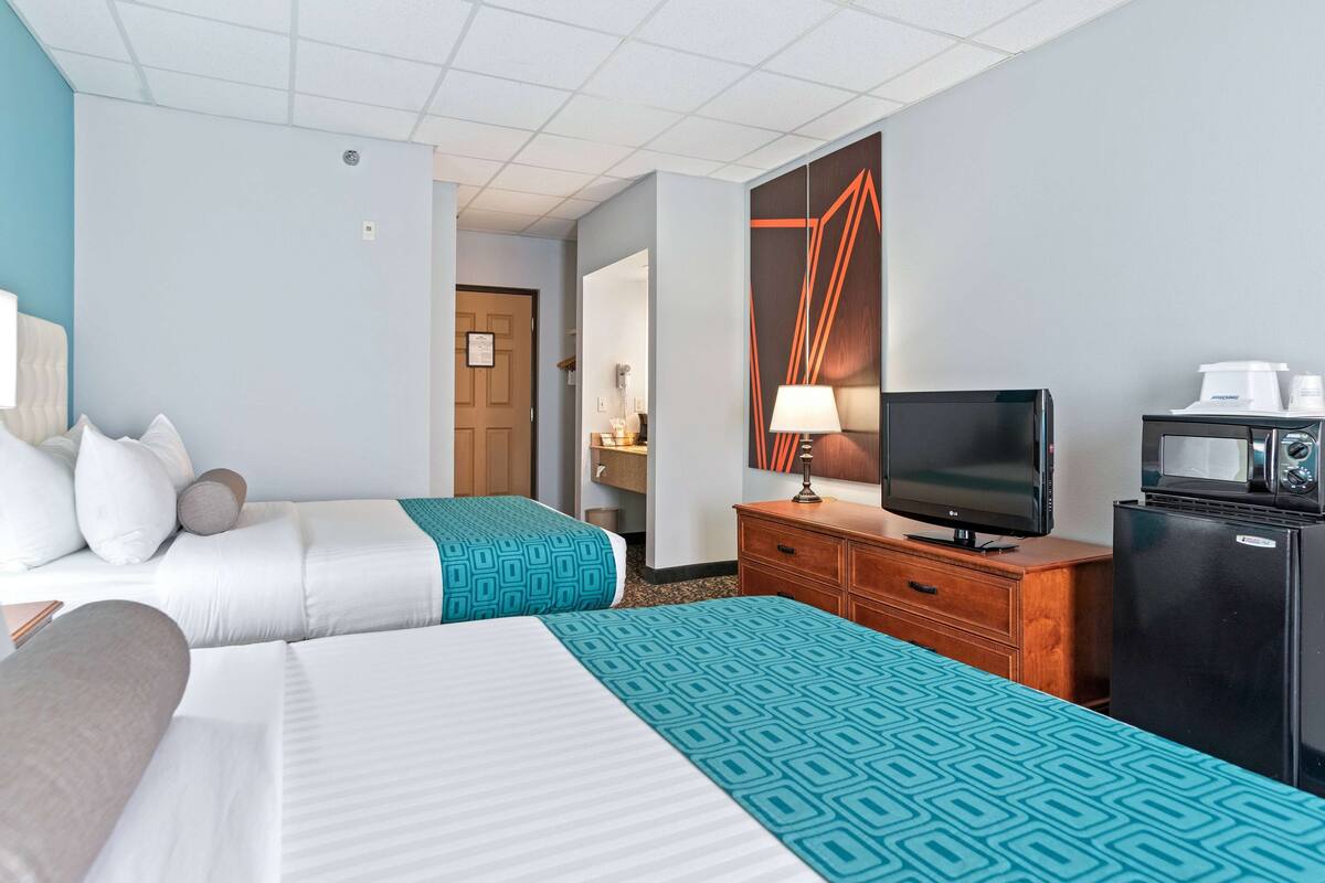Ein Hotelzimmer mit zwei Betten, einem Fernseher, einem Kühlschrank und einer Mikrowelle.