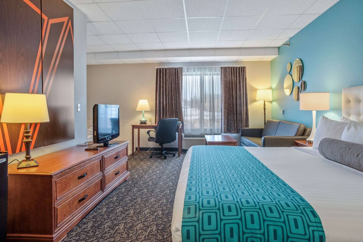 Ein Hotelzimmer mit Bett, Schreibtisch, Stuhl, Fernseher und einem Fenster mit Vorhängen.