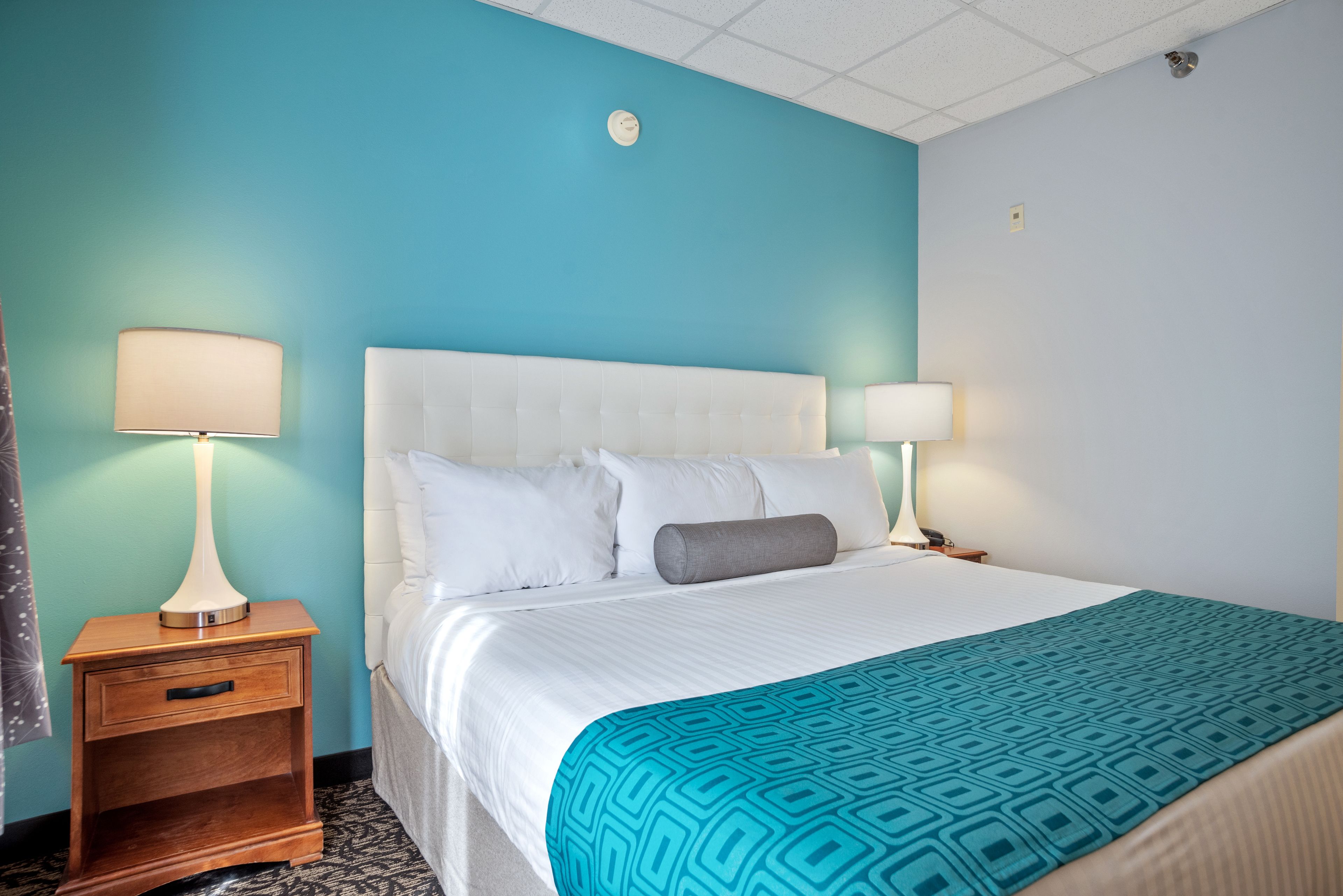 Habitación de hotel con una cama blanca, dos lámparas de noche, una mesita de noche de madera y una pared de acento color aguamarina.
