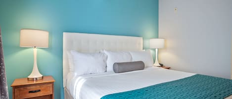 A hotel room with a white bed, two bedside lamps, a wooden nightstand, and a teal accent wall.