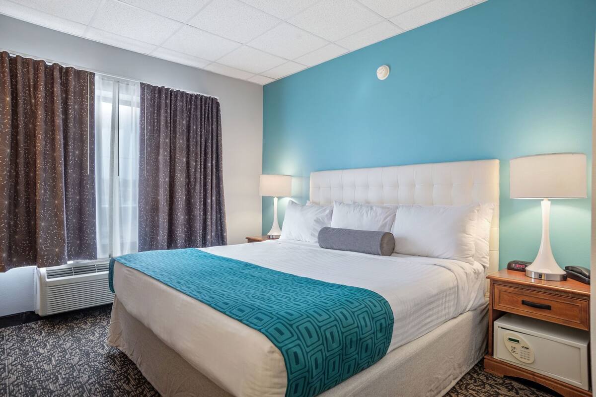 Ein Hotelzimmer mit einem Bett, zwei Nachttischlampen, einem Nachttisch, einer digitalen Uhr und einem Thermostat.