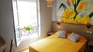 Un dormitorio con cama, ventana, un cuadro y una araña.