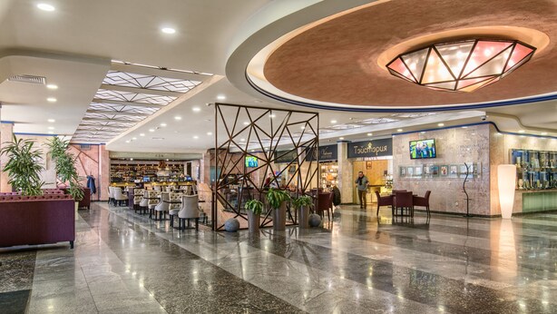 A spacious lobby with a modern design, featuring a central seating area, a bar, and a display wall with photos. - President Hotel (Kyiv)
