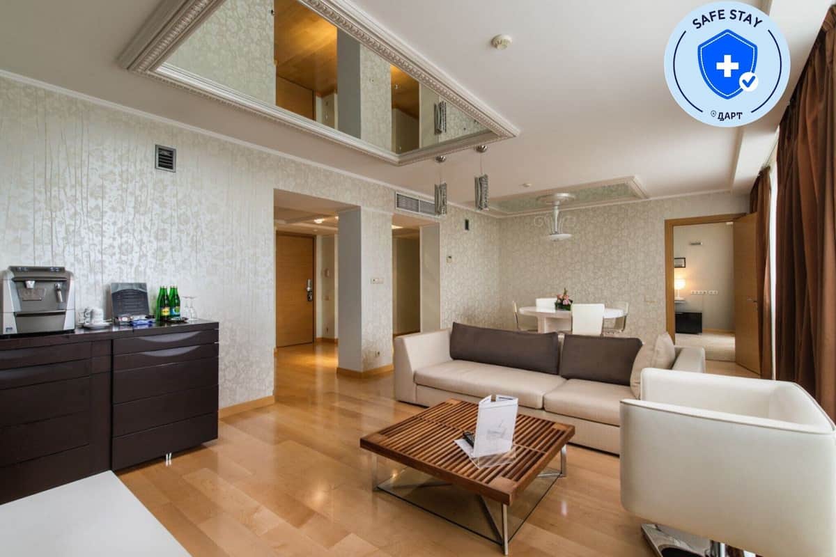 A modern hotel room with a sofa, a coffee table, a desk with a computer, and a mirror.
