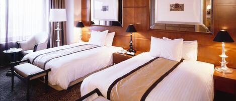 A hotel room with two beds, a sitting area, and a desk.