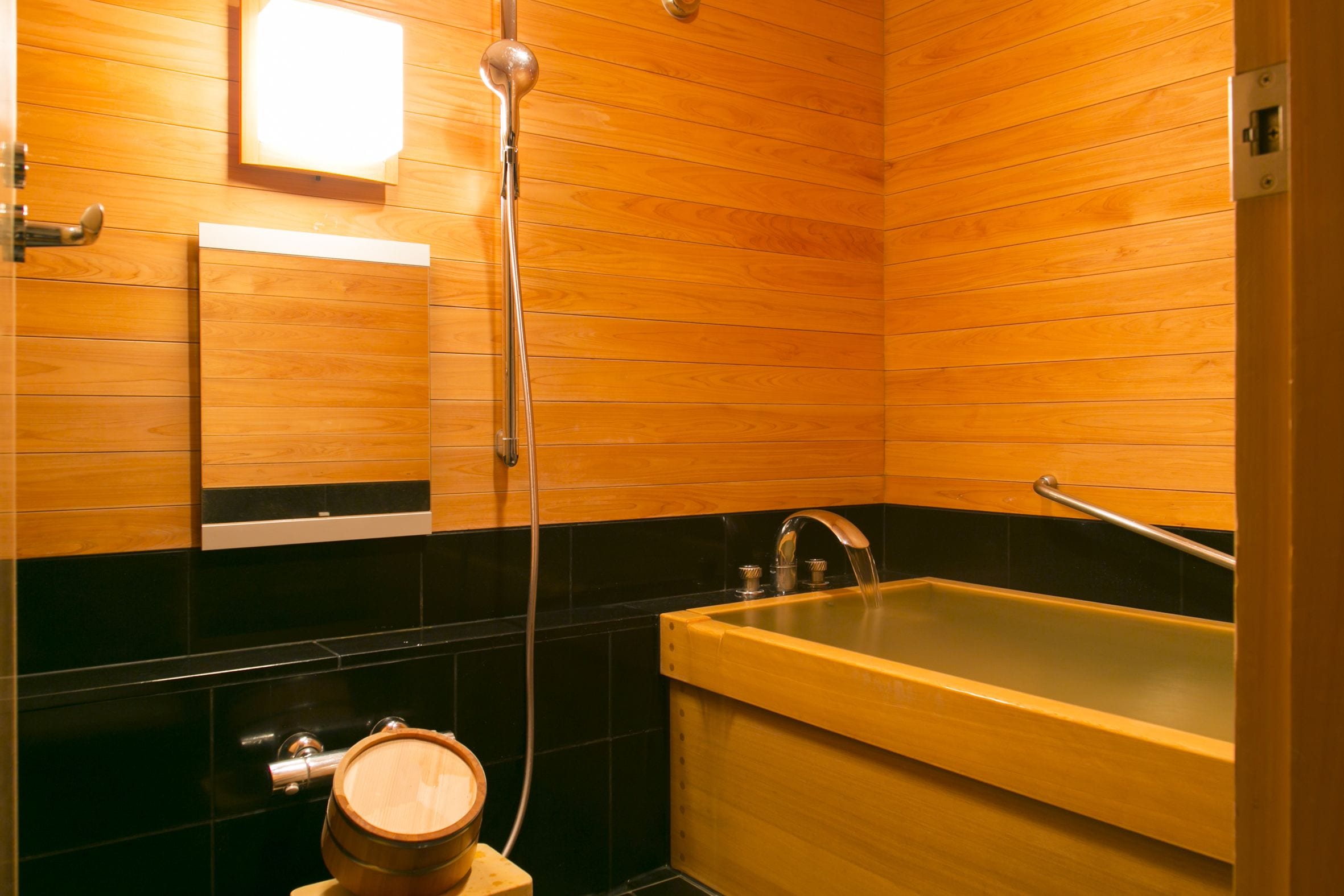 A wooden-paneled bathroom with a bathtub, a wooden barrel, and a mirror.