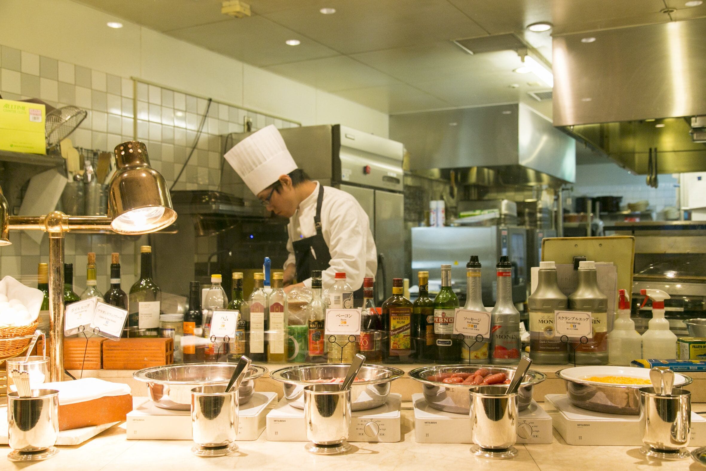 A chef preparing food in a commercial kitchen with various cooking utensils, ingredients, and kitchen equipment.