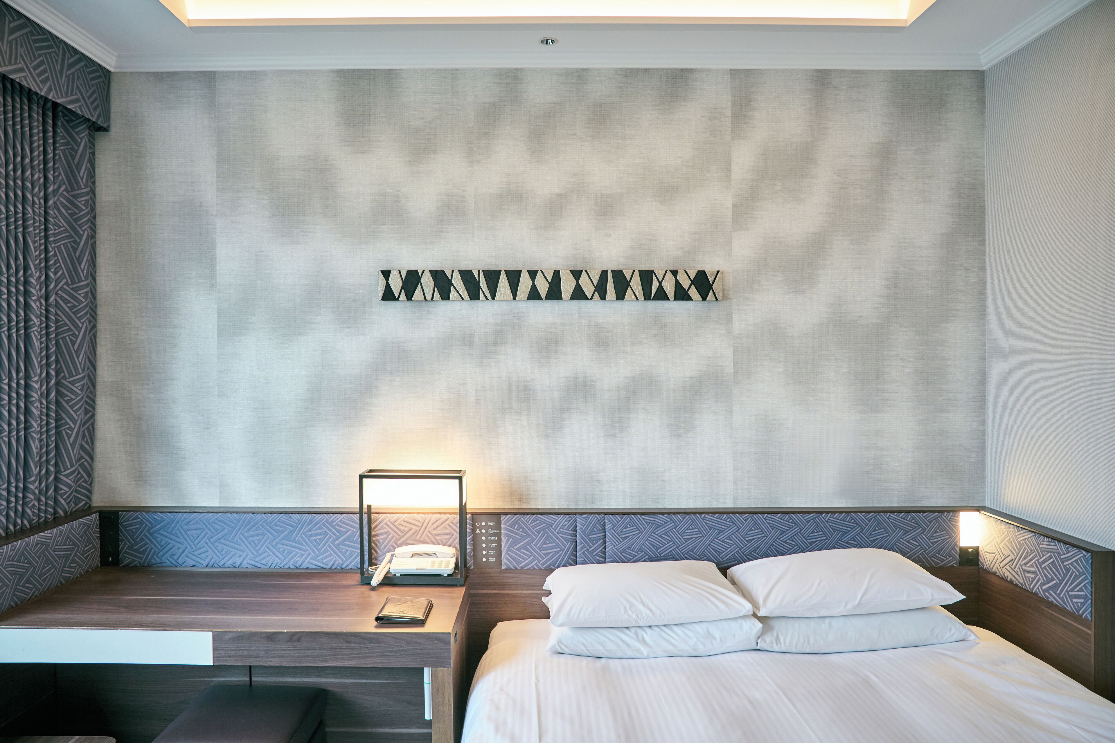 A hotel room with a bed, bedside table, and a wall-mounted telephone.