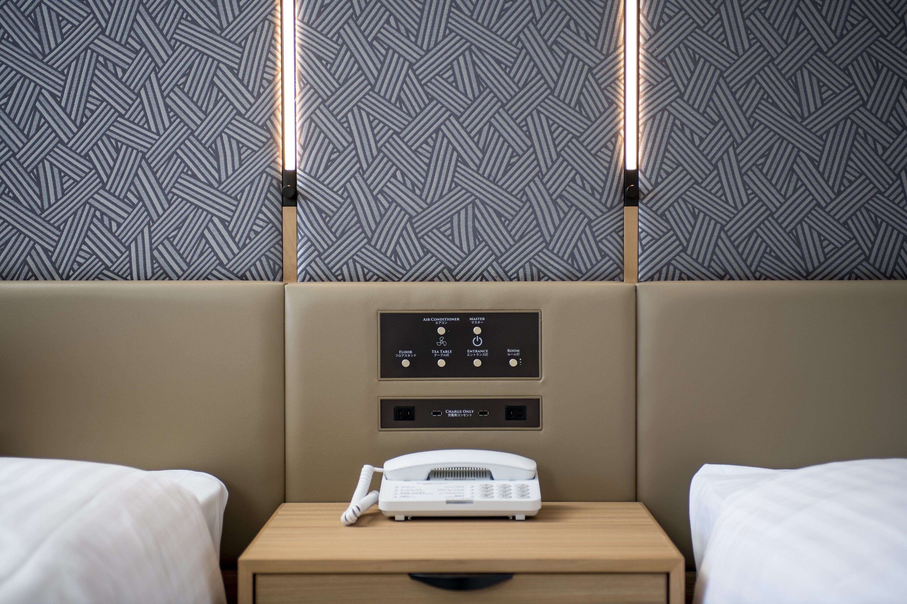 Habitación de hotel con dos camas, una mesita de noche con teléfono y panel de control para aire acondicionado y otros servicios.