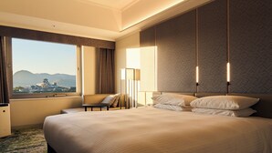A hotel room with a large bed, a desk, and a view of a building through a window. - Hotel Nikko Kumamoto (Kumamoto)