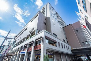 Un hotel moderno con una entrada destacada, varios pisos y un cielo despejado.