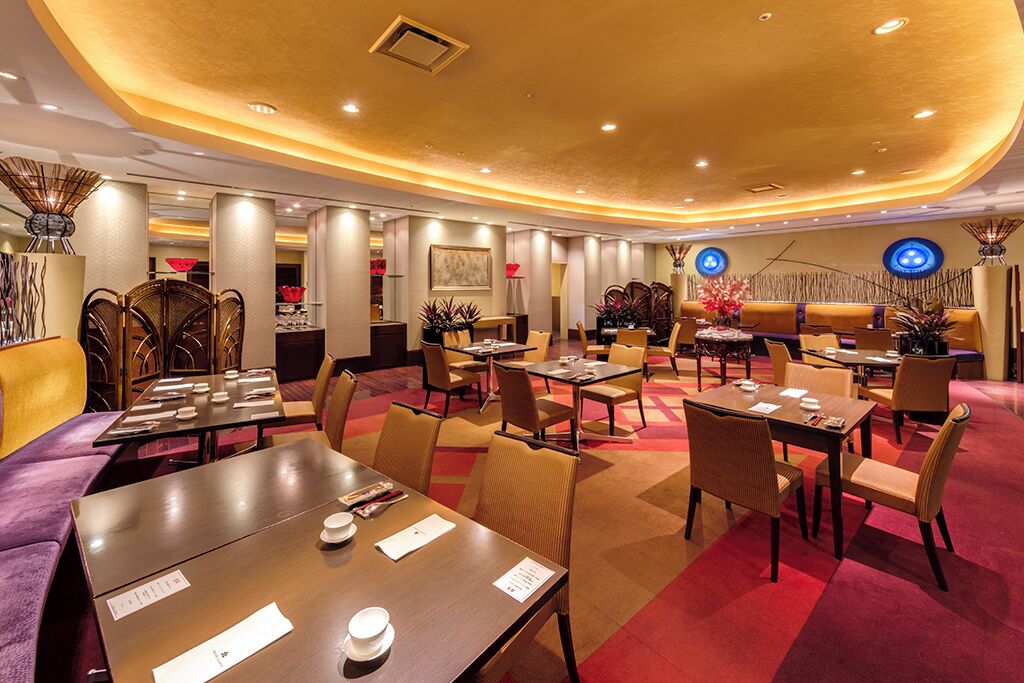 A hotel lobby with multiple seating areas, including a reception desk, several tables and chairs, and decorative plants.