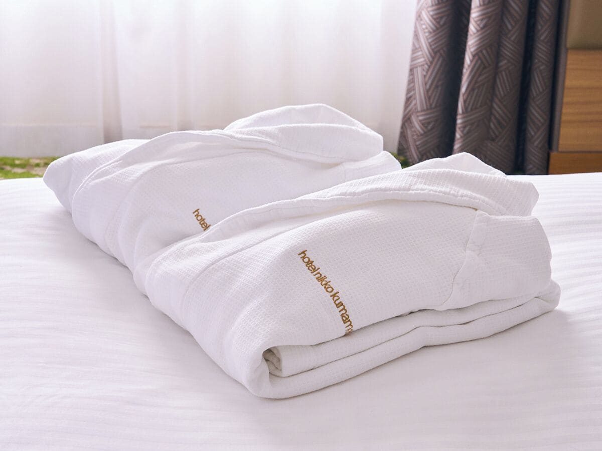 A neatly folded white towel with "hotel niko kumano" text on it, placed on a bed with white bedding.