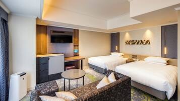 A hotel room with two beds, a sofa, a desk with a TV, and a minibar.