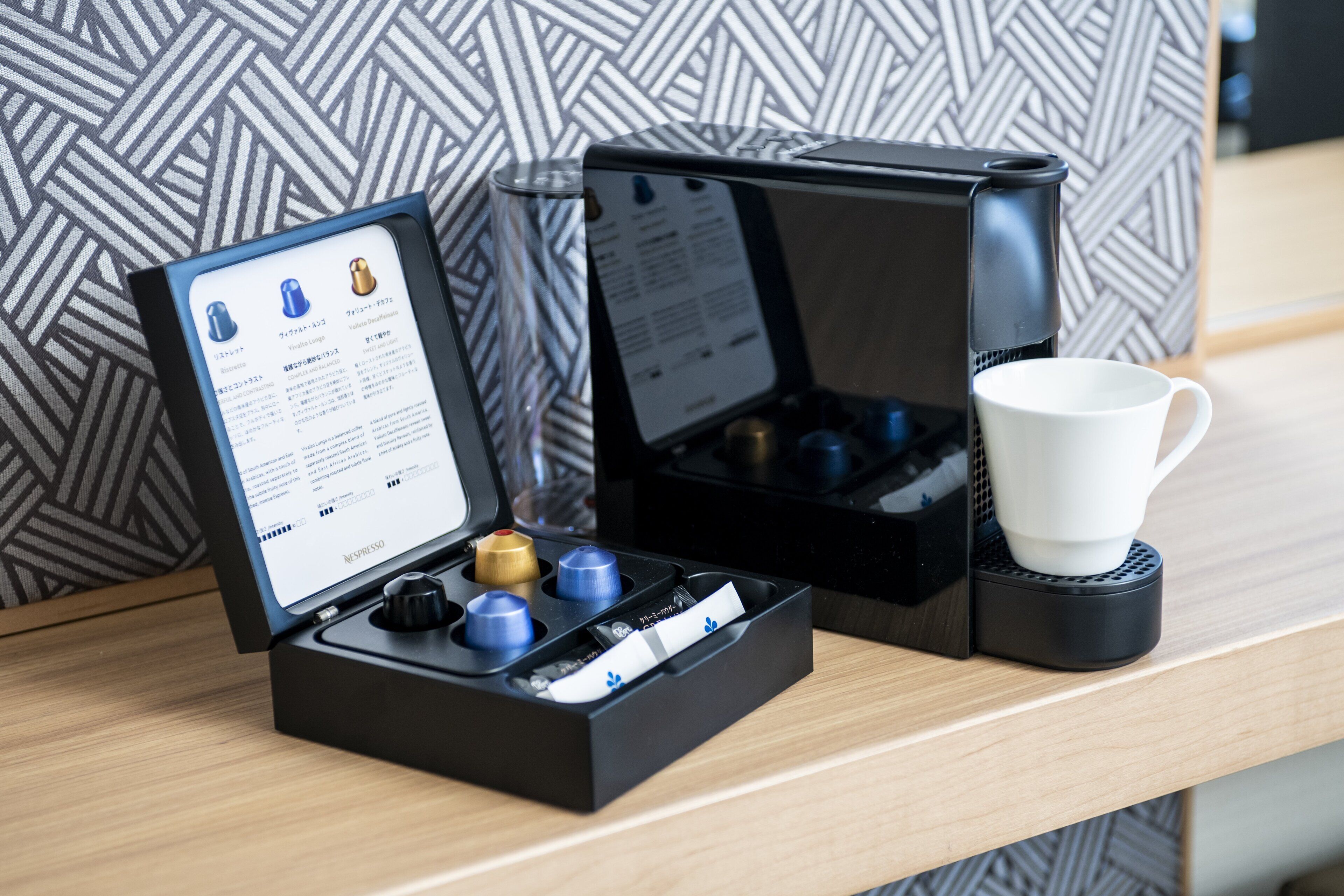 A coffee maker with a manual and a cup on a wooden surface.