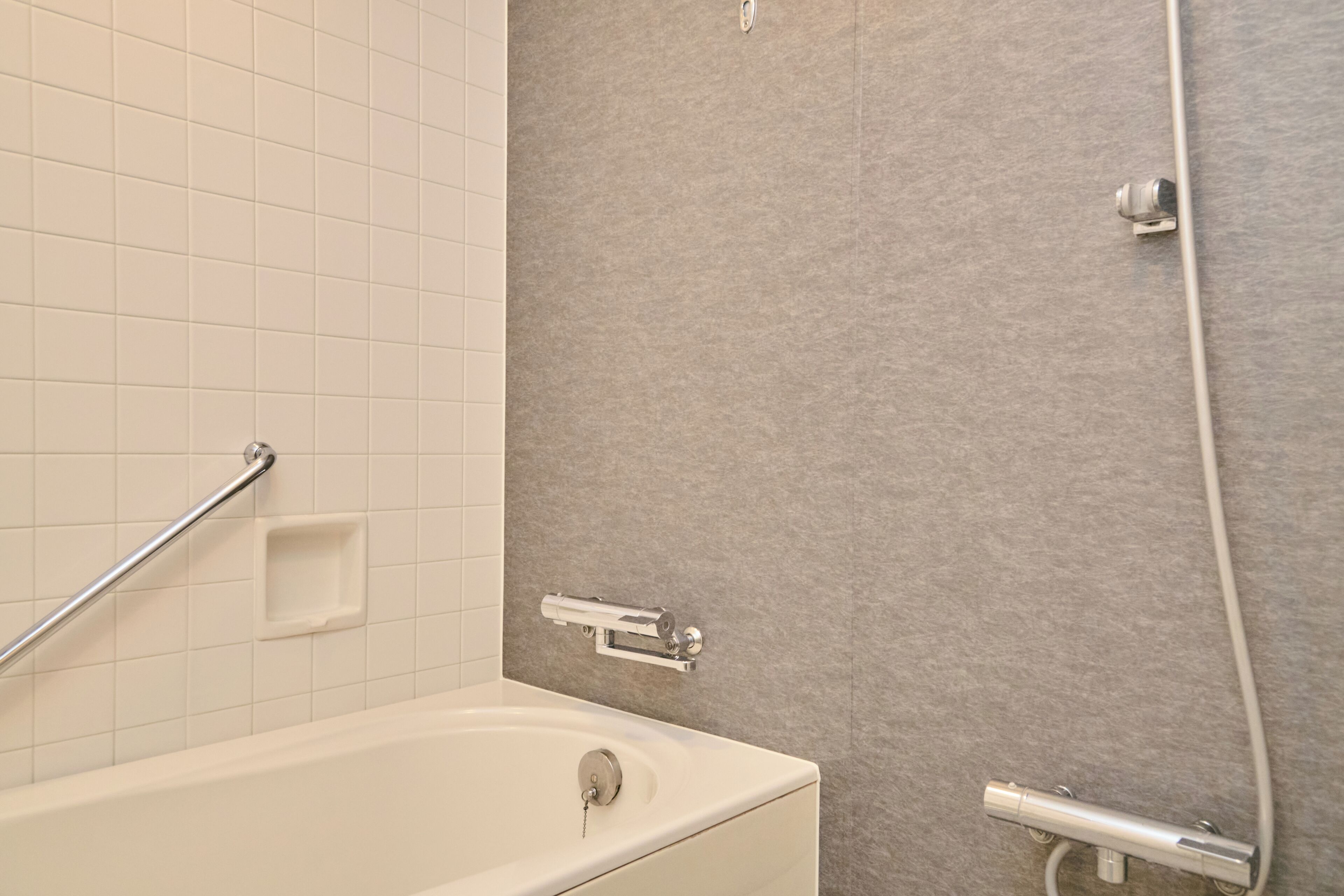 Une salle de bain avec une baignoire blanche, une douche dotée d’une porte en verre et une barre d’appui.