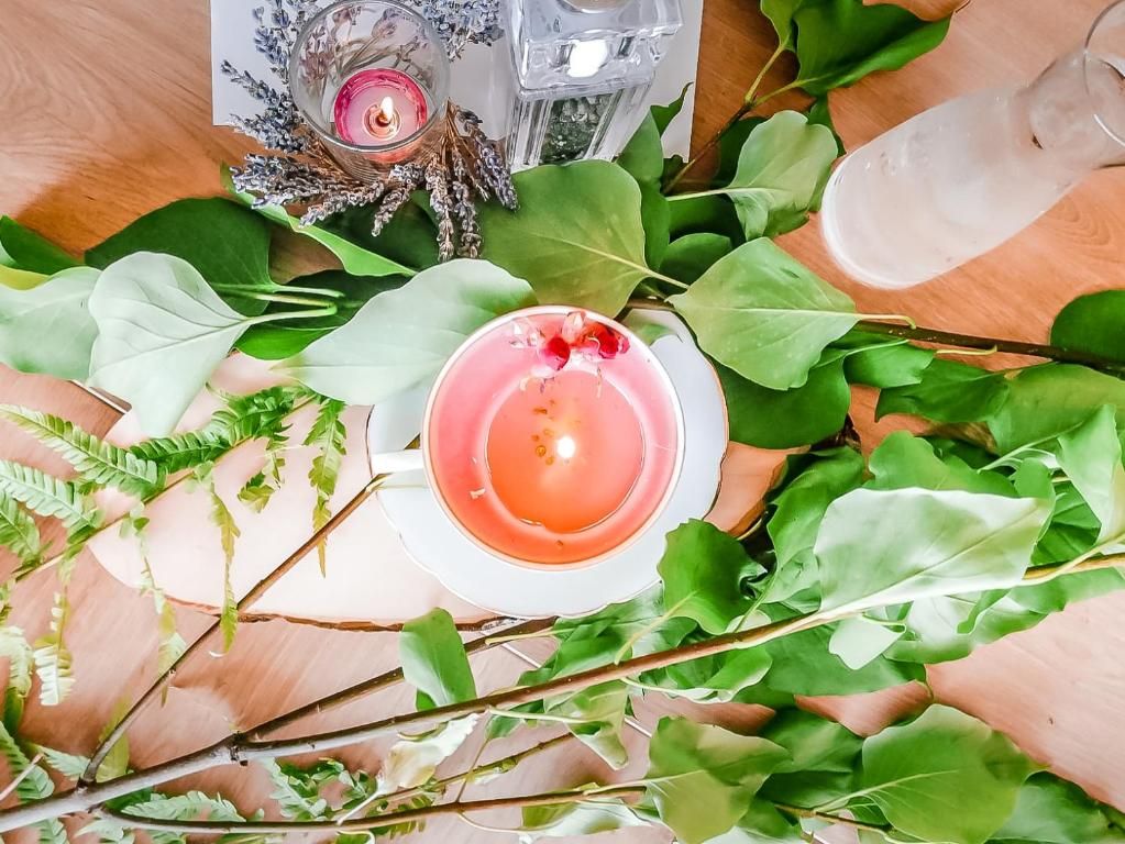 Ett bord med ett ljus, ett glas vatten och gröna löv.