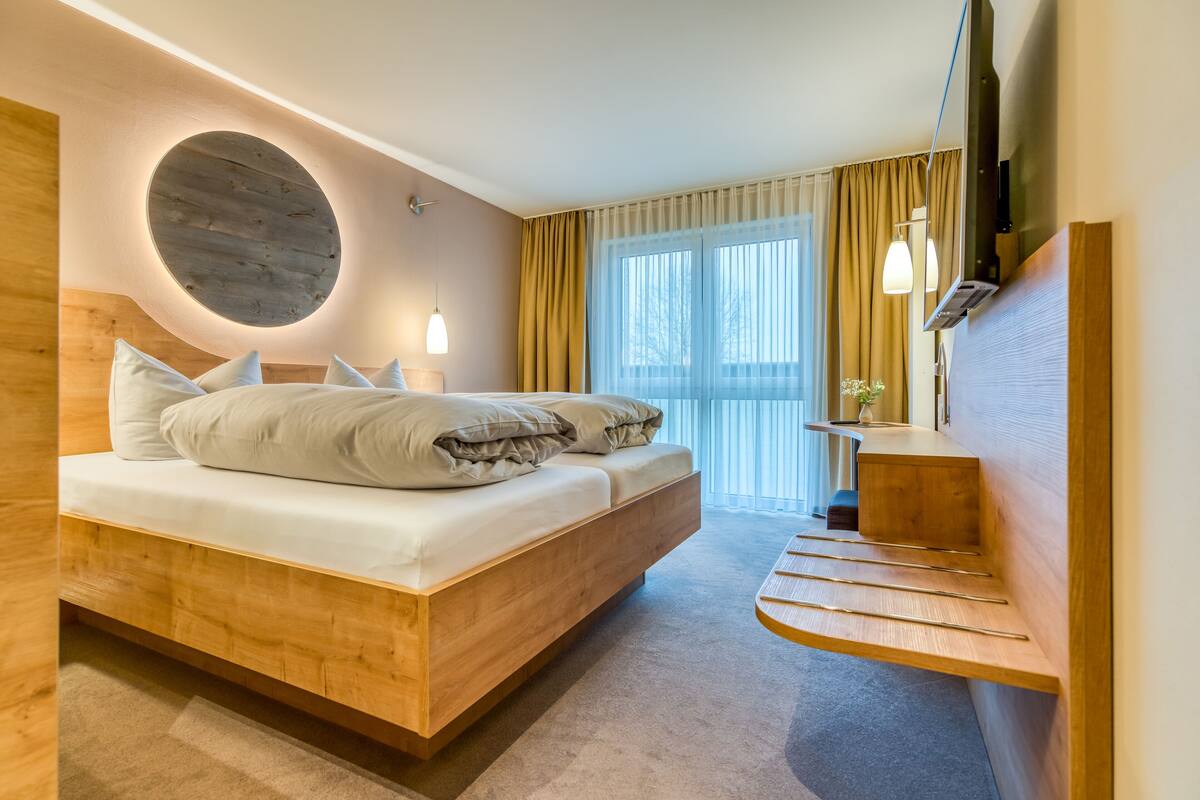 A modern hotel room with a wooden bed, a round wall feature, and a built-in TV.