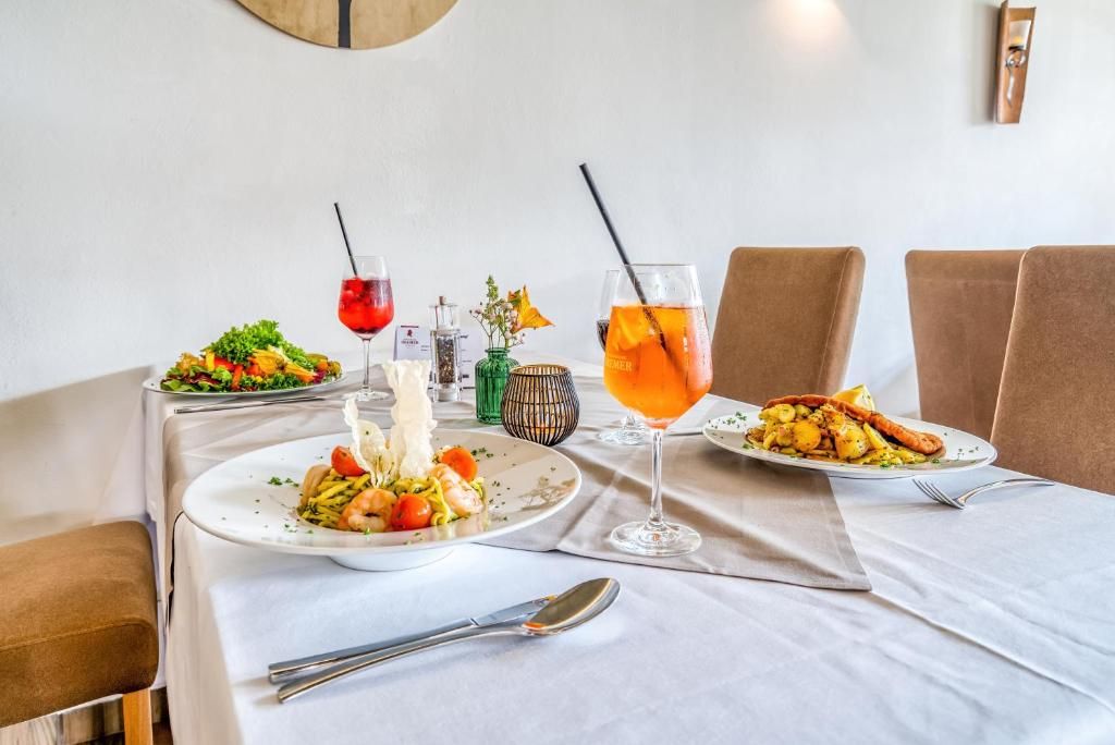 A dining table with two plates of food, two drinks, and a spoon.