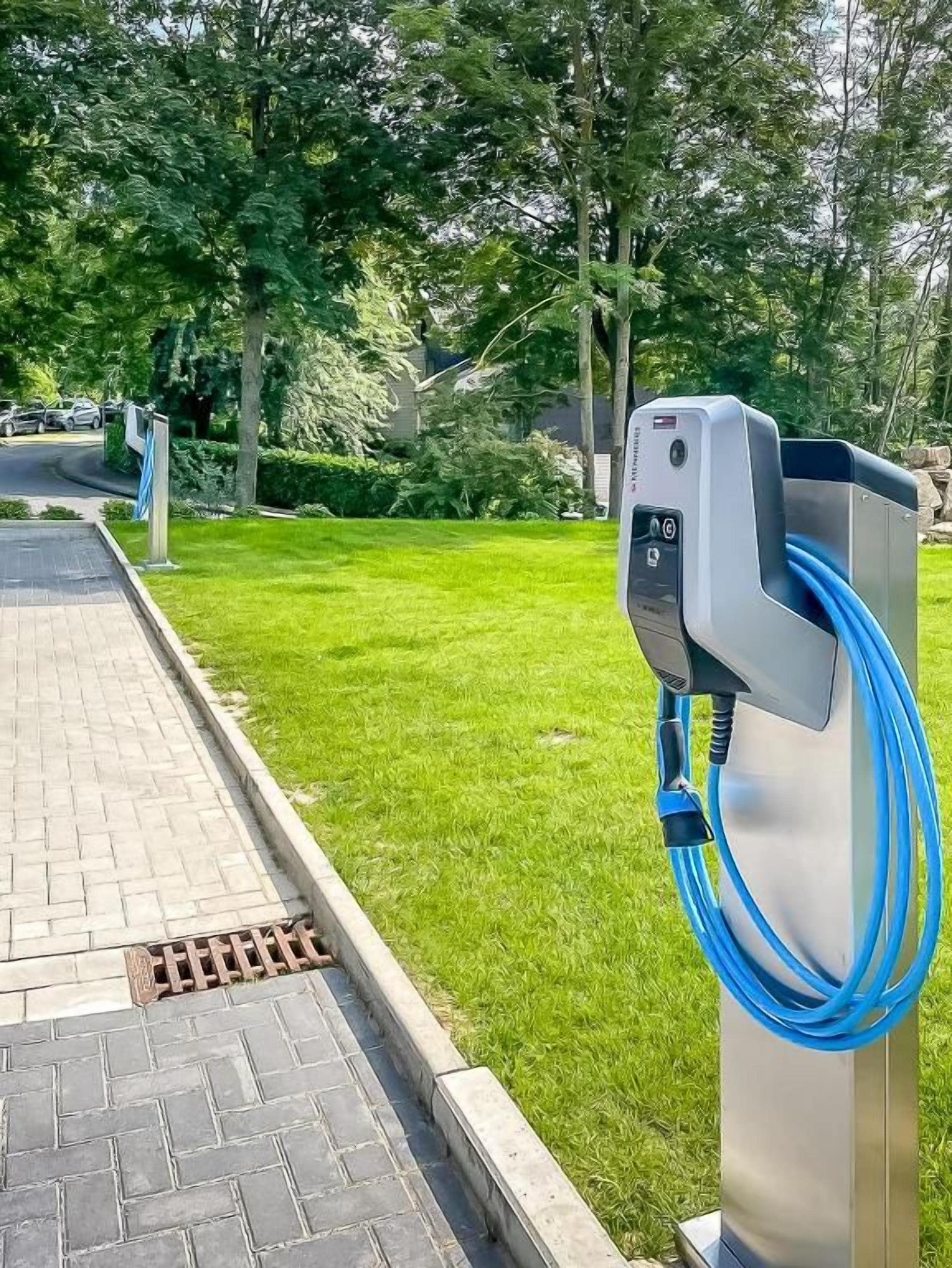 Eine Ladestation für Elektroautos mit einem blauen Kabel, eingebettet in eine grüne Wiese mit einem befestigten Weg in der Nähe.