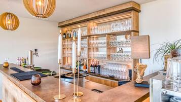 Eine Bar mit einer Holztresen, Regalen für Gläser und Flaschen sowie Pendelleuchten.